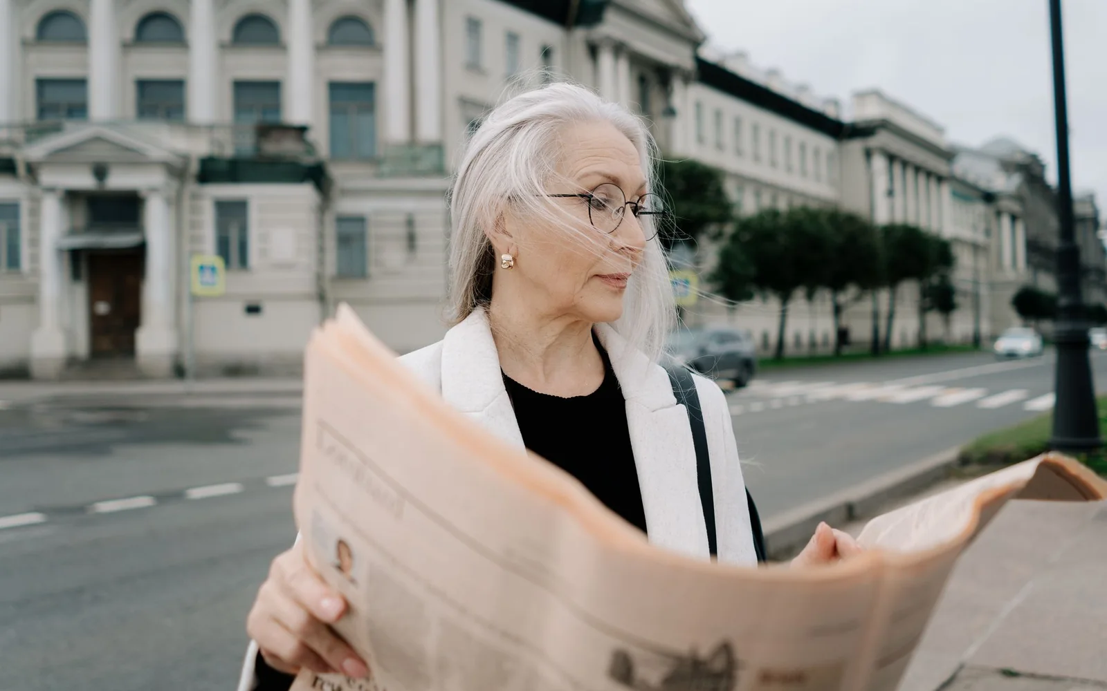 Persoană care citește cu ochelari într-un cadru urban